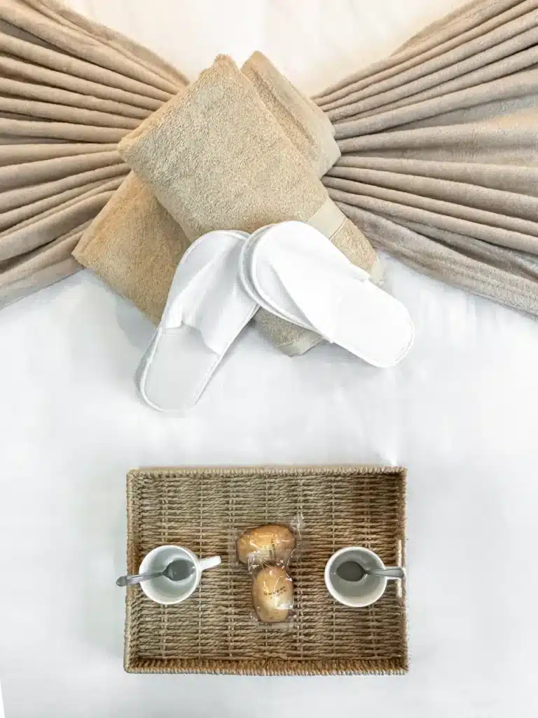 Plateau en osier, tasses blanches, serviettes pliées et chaussons, vus d’en haut
