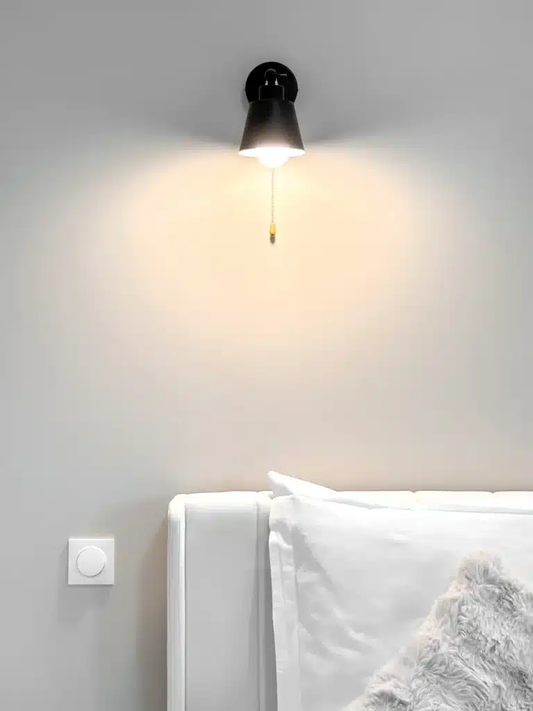Applique murale noire allumée au-dessus d’une tête de lit blanche